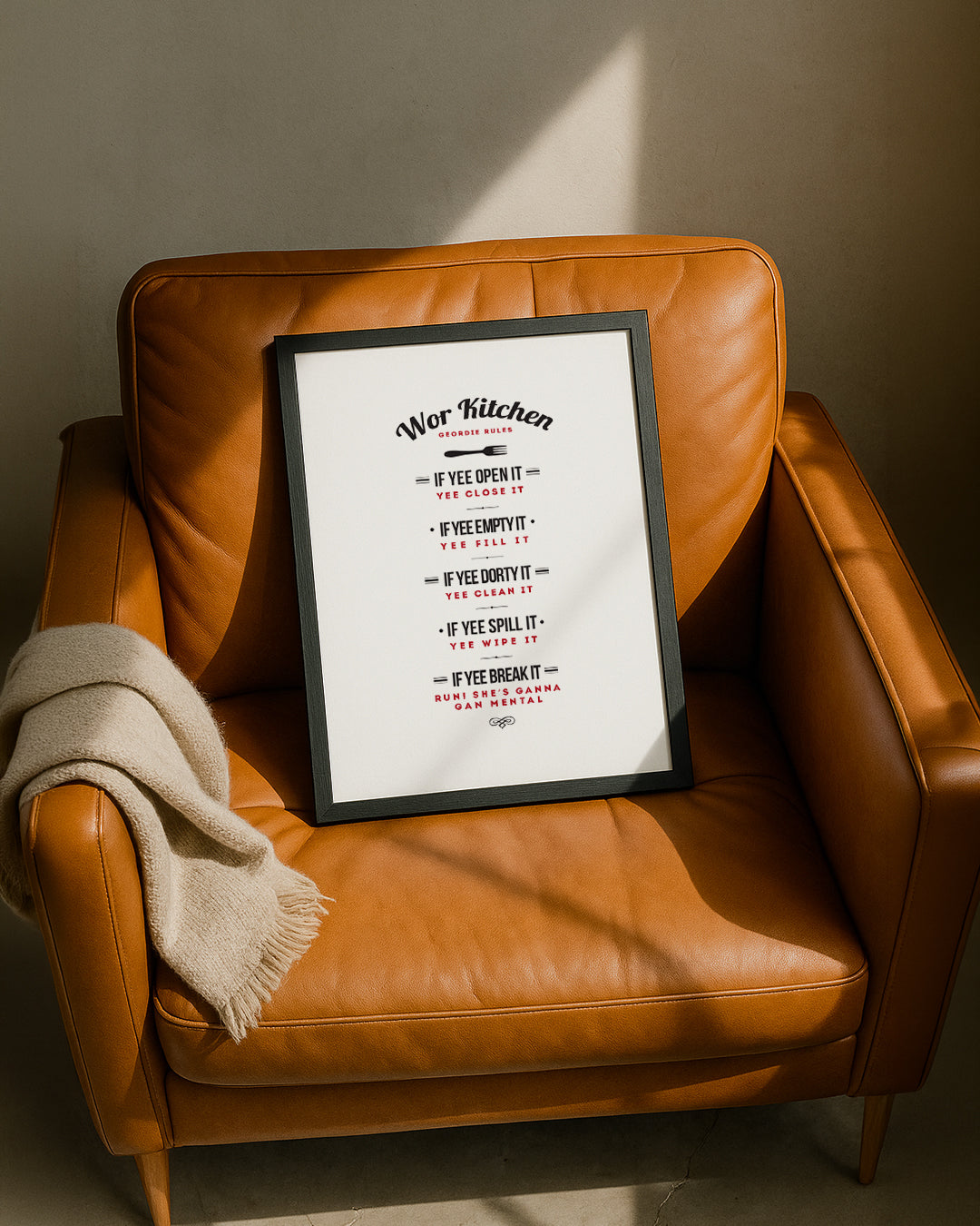 The 'Wor Kitchen' Geordie dialect print leaning against a tan leather armchair.