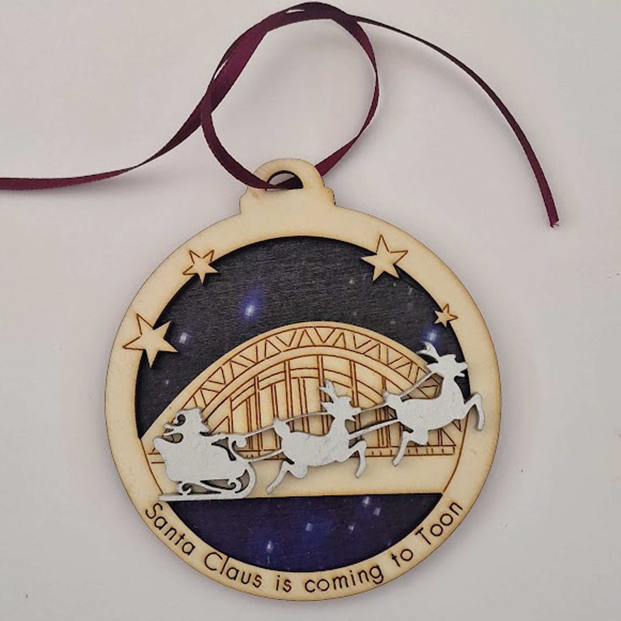 Unique High Quality Lazer Cut Geordie Christmas Tree Decoration Baubles Bauble displays: Etched illustration of the Tyne Bridge with Santa & his reindeers flying past alongside the wording 'santa claus is coming to Toon' Dimensions: 9 x 9cm. Each bauble is supplied with ribbon