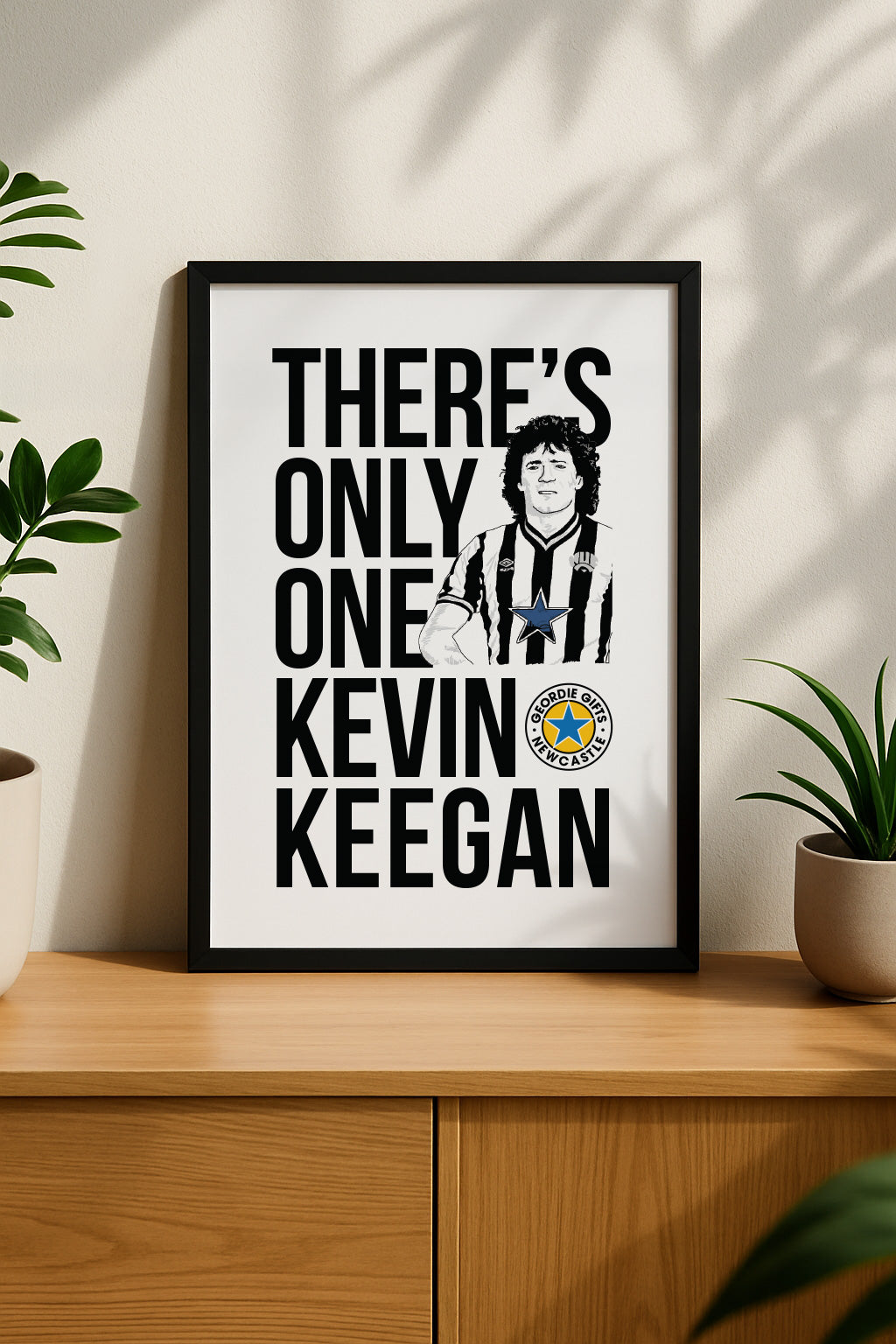Black framed "There's Only One Kevin Keegan" Newcastle United football chant print by Geordie Gifts styled on a wooden sideboard.