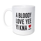 White ceramic coffee mug featuring the text 'A BLOODY LOVE YEE YI KNA' in black with a small red heart. Funny Geordie Valentine's gift designed by Geordie Gifts.