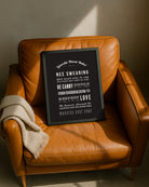 Framed "Geordie Hoose Rules" typography poster resting casually on a tan leather armchair next to a folded beige throw blanket, illuminated by warm sunlight. Designed for Geordie Gifts.