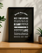 Framed "Geordie Hoose Rules" Newcastle slang wall art resting on a modern wooden sideboard, styled with green house plants on either side with natural leaf shadows cast on the beige wall behind it. Designed for Geordie Gifts.