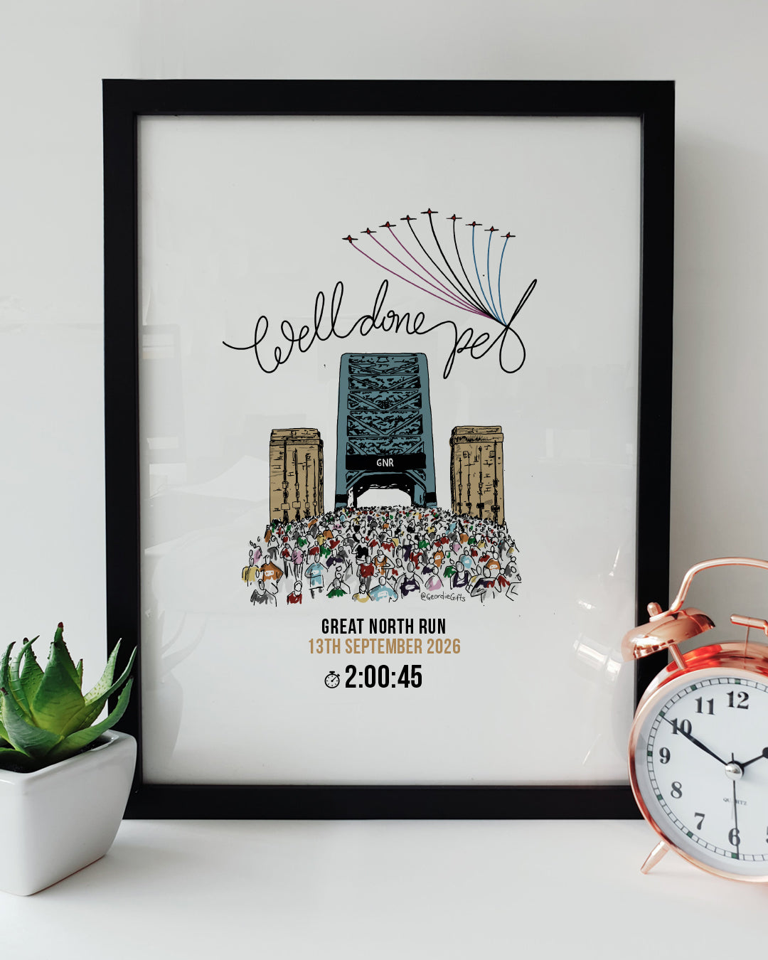 Personalised Great North Run wall art print reading "Well done pet" featuring Tyne Bridge illustration and custom finish time in a black frame next to an alarm clock designed by geordie gifts