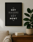 A bold black Geordie Gifts print with white 'Shy Bairns Get Nowt' text sitting on a wooden sideboard.