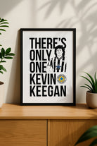 Black framed "There's Only One Kevin Keegan" Newcastle United football chant print by Geordie Gifts styled on a wooden sideboard.