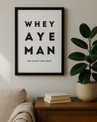 The "Whey Aye Man" Geordie Gifts wall art sitting on a wooden sideboard, featuring minimalist black and white Newcastle dialect design.
