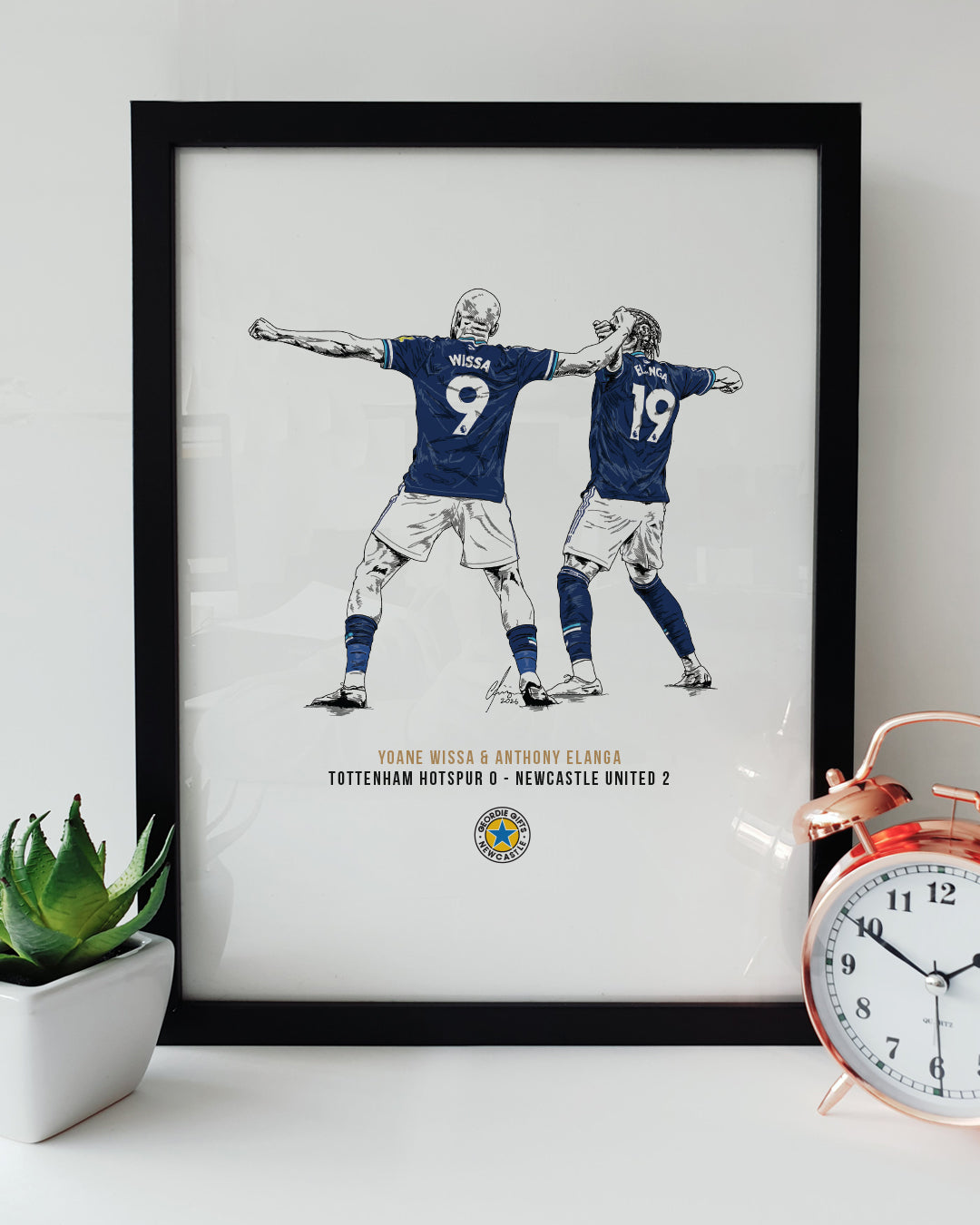 Black framed Yoane Wissa and Anthony Elanga Tottenham 0-2 Newcastle celebration print by Geordie Gifts styled next to a rose gold alarm clock.