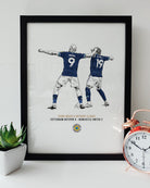 Black framed Yoane Wissa and Anthony Elanga Tottenham 0-2 Newcastle celebration print by Geordie Gifts styled next to a rose gold alarm clock.